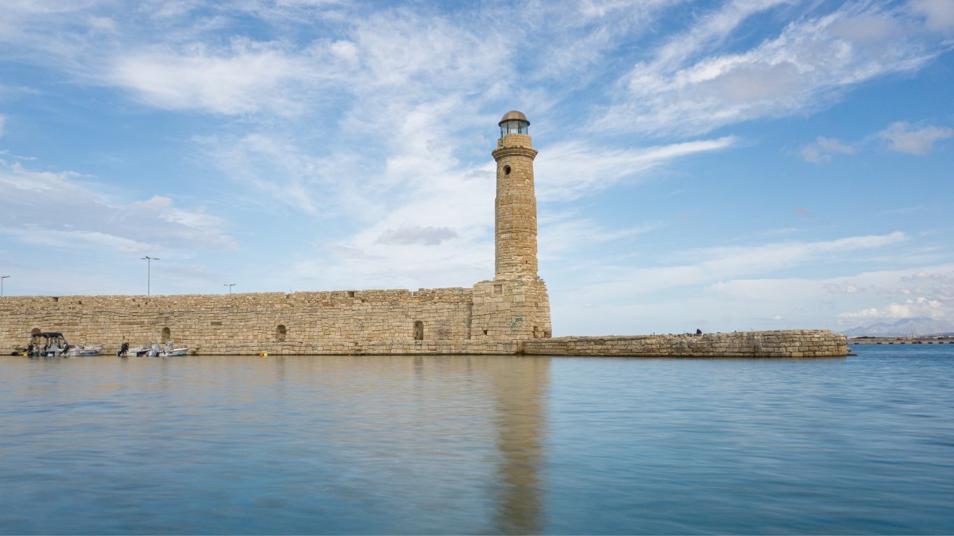 De vuurtoren staat trots aan het uiteinde van de kade, omringd door vissersbootjes, cafés en tavernes. Het is een plek waar je de zonsondergang kunt bewonderen met uitzicht op de azuurblauwe zee.